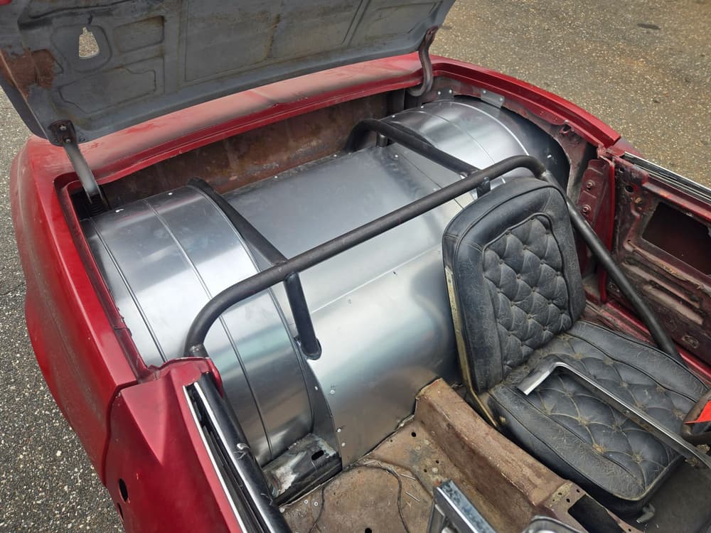 Custom fabricated aluminum fuel tank installed in the trunk of a classic convertible behind a welded roll bar.