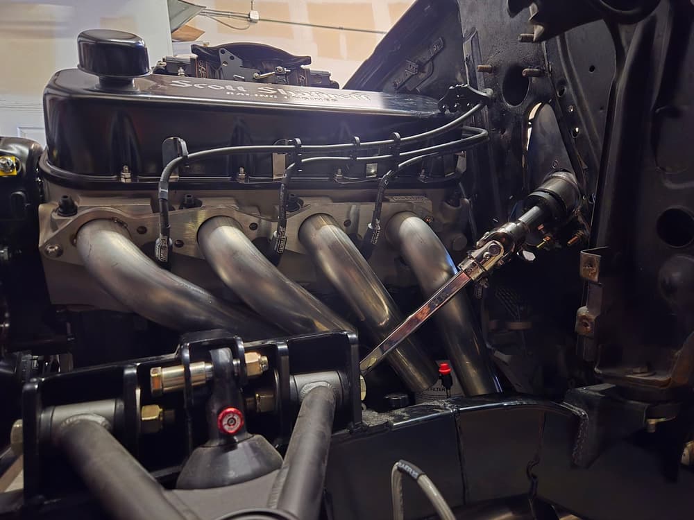 Race car engine bay showing fabricated stainless steel headers and a welded tube chassis.
