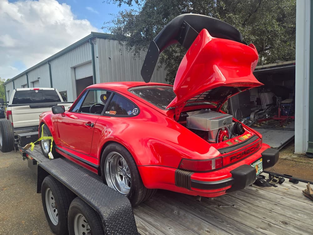 Red Porsche 911 on a trailer at the Jacksonville welding shop with the engine lid open.